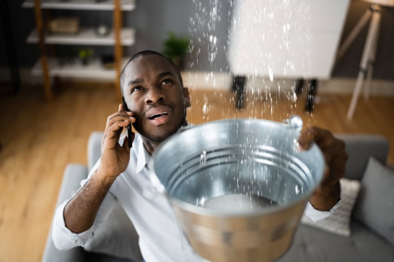 Man on phone holding a bucket under a drip.