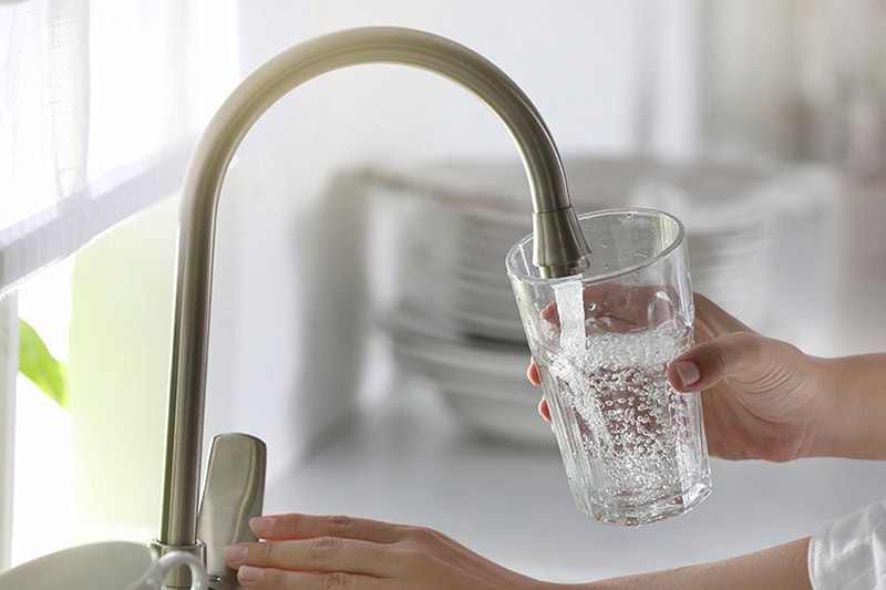 The Impact of Hard Water on Your Plumbing System. Water coming out of a faucet into a glass.